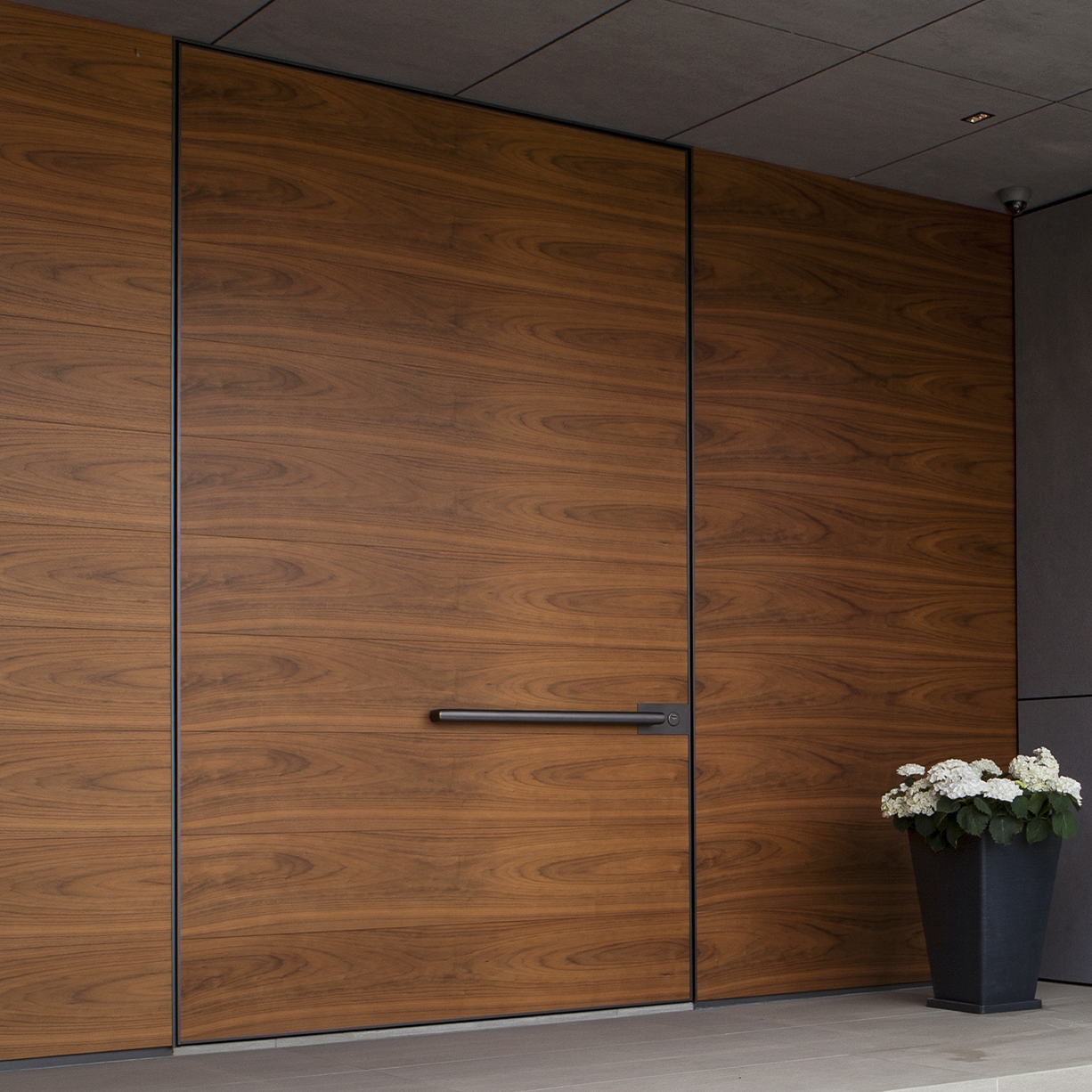 Display product Synua | The safety door for large dimensions, with vertical pivot operation and installation coplanar with the wall. from manufacturer Oikos Venezia – Architetture d’ingresso