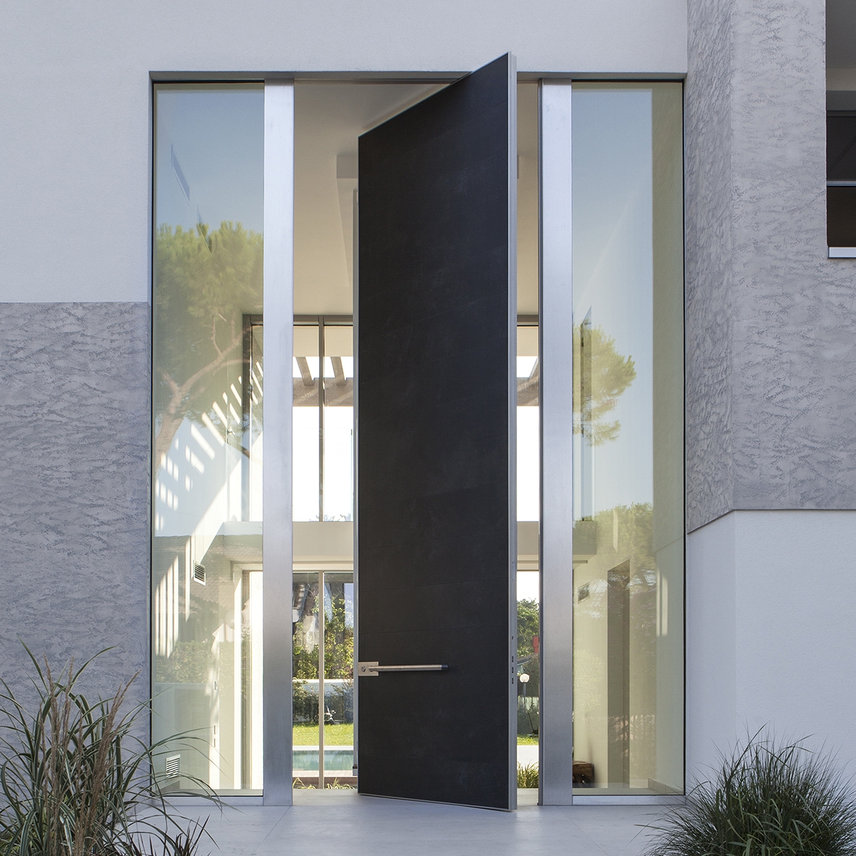 Display product Synua | The safety door for large dimensions, with vertical pivot operation and installation coplanar with the wall. from manufacturer Oikos Venezia – Architetture d’ingresso