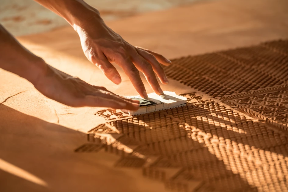 American artist Rena Detrixhe first spreads out fine red earth evenly into a rectangular shape to create a temporary carpet before using parts of soles from old shoes to emboss fine patterns and ornaments into her "Red Dirt Rug"