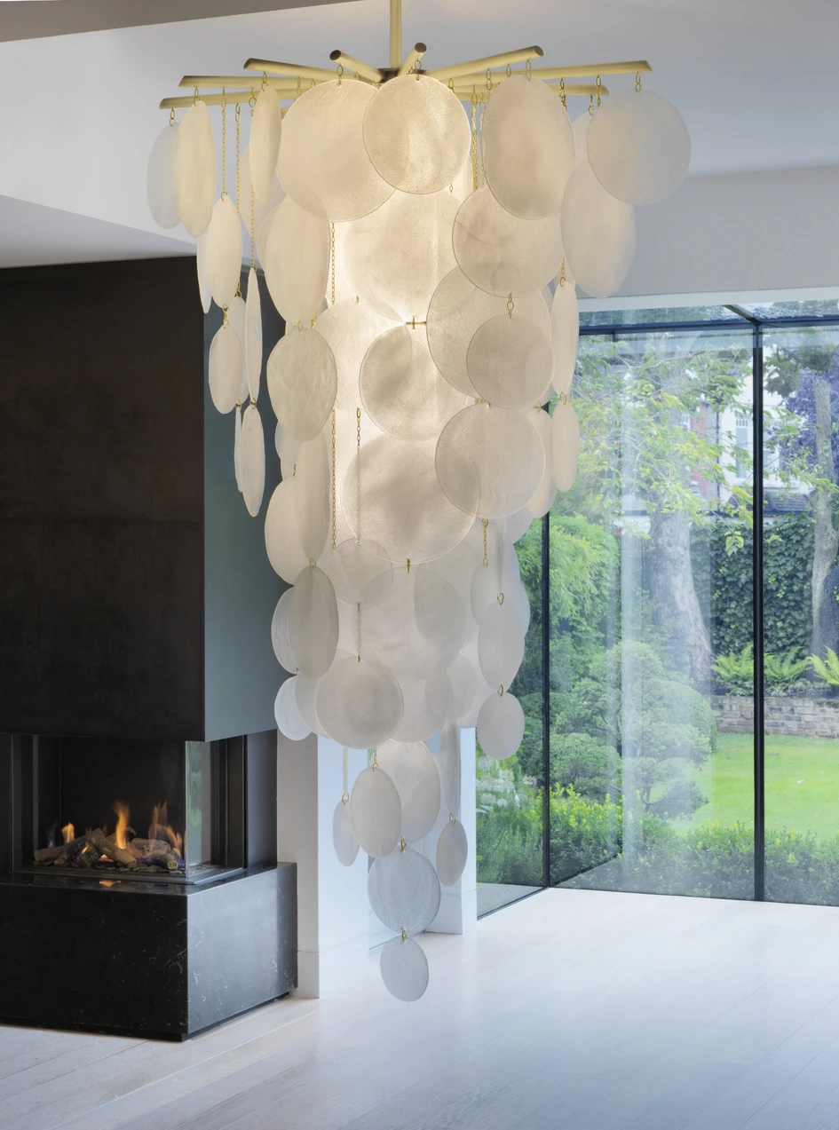 A cloud of handcrafted glass discs hangs from a bronze frame in the Nimbus chandelier and cascade lights