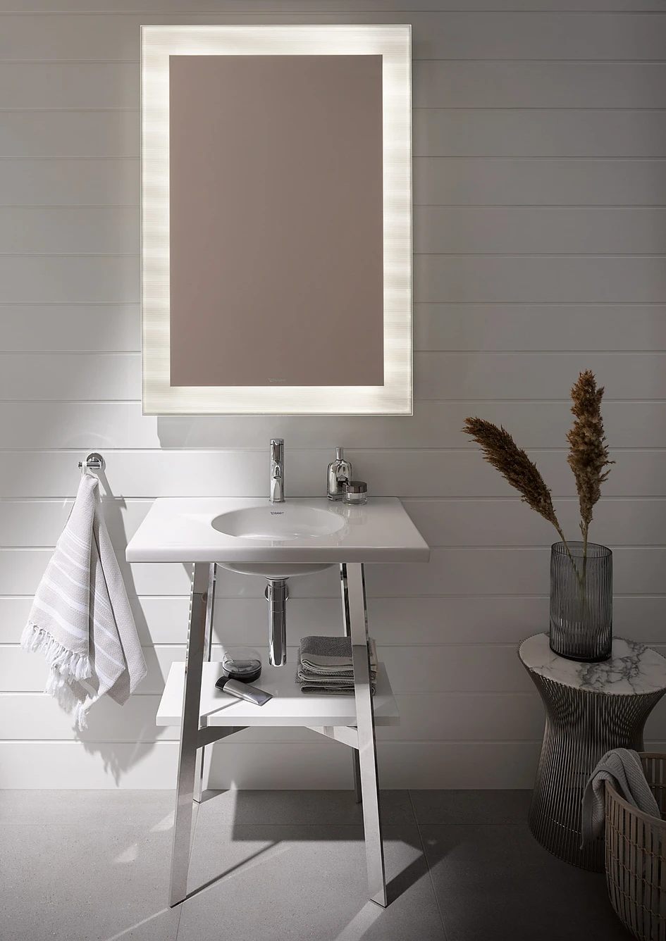 The combination of the washbasin in glossy white ceramic with the floor-standing chrome frame looks elegant and puristic. The wide shelves on the right and left are both practical and easy to clean