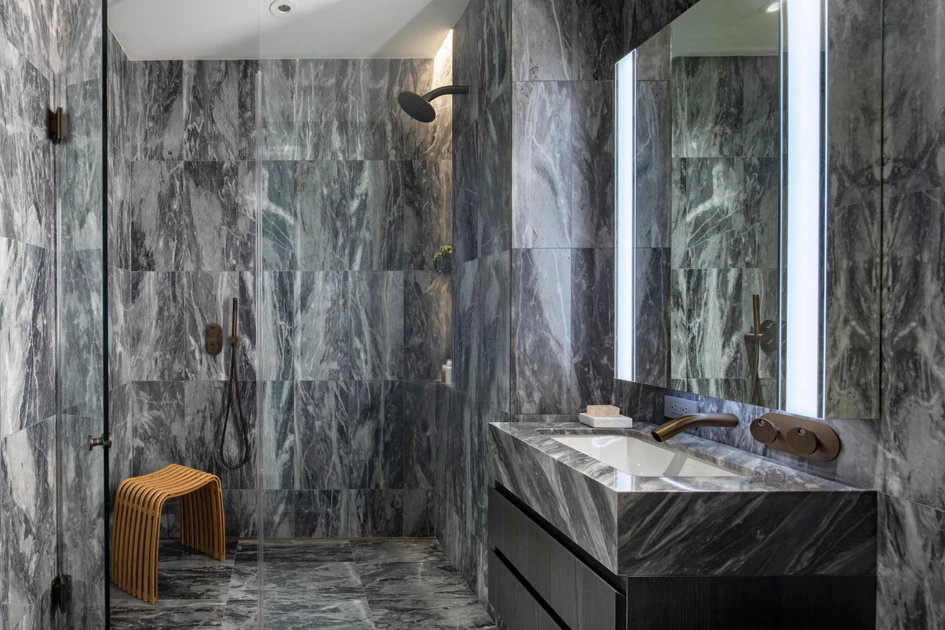 The secondary bathroom in the model residences features floor-to-ceiling Salvatori-honed Grigio Versilia marble and Adjaye’s custom-designed faucets and showerheads in a burnished bronze finish