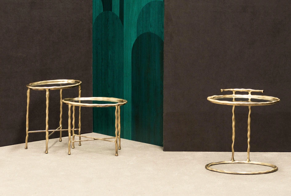 The curves of the upholstered pieces are matched by those of the collection’s new side tables. Lupa’s textured cast brass legs and frame support a circular glass top
