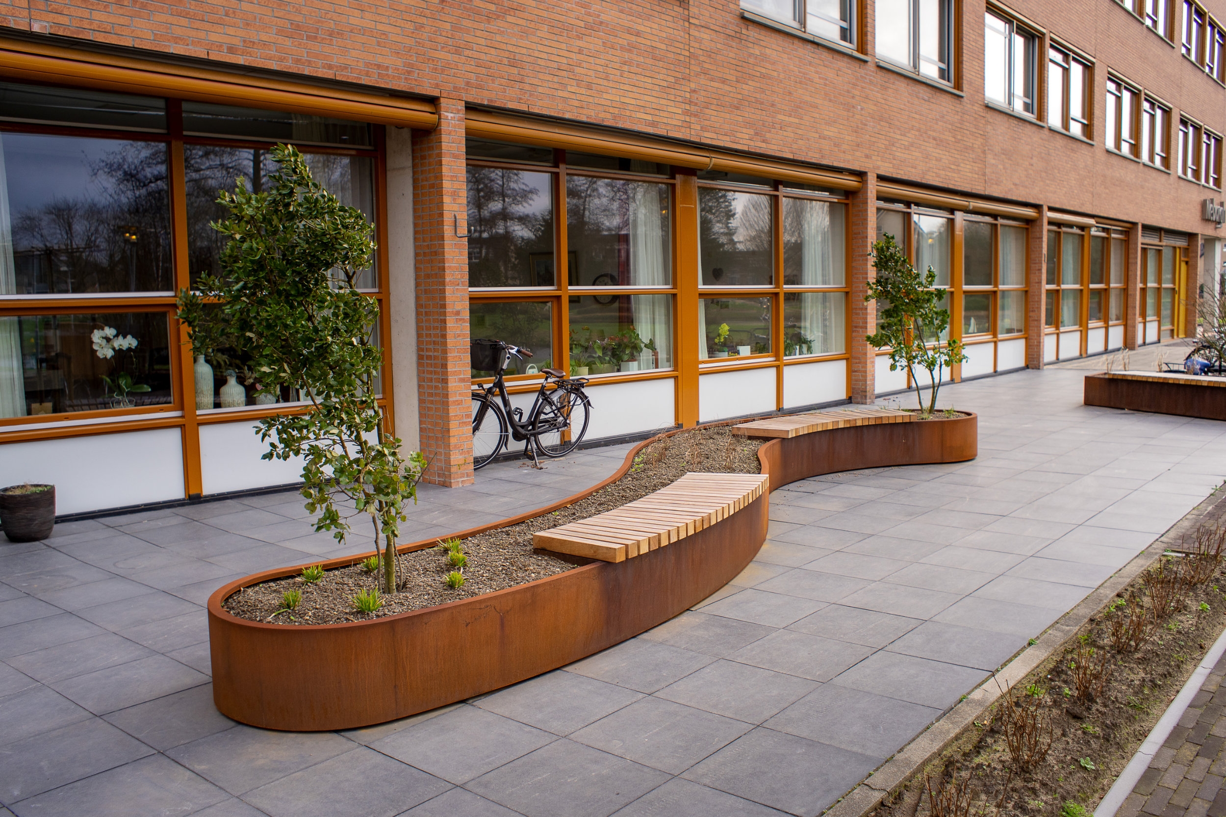 Slatted wooden benches are creatively incorporated into retaining walls made from Corten steel at the new AFAS Experience Centre in Leusden (top) and at a care home in Zwijndrecht