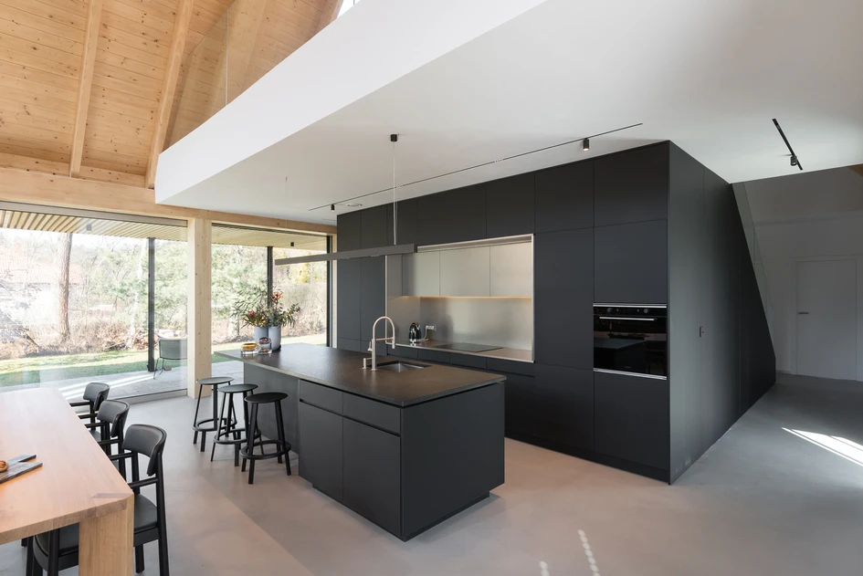 The Ode to Nature House’s dark kitchen and stone fireplace wall bookend its cavernous, light-filled central living space. Photos: Przelysław Turlej