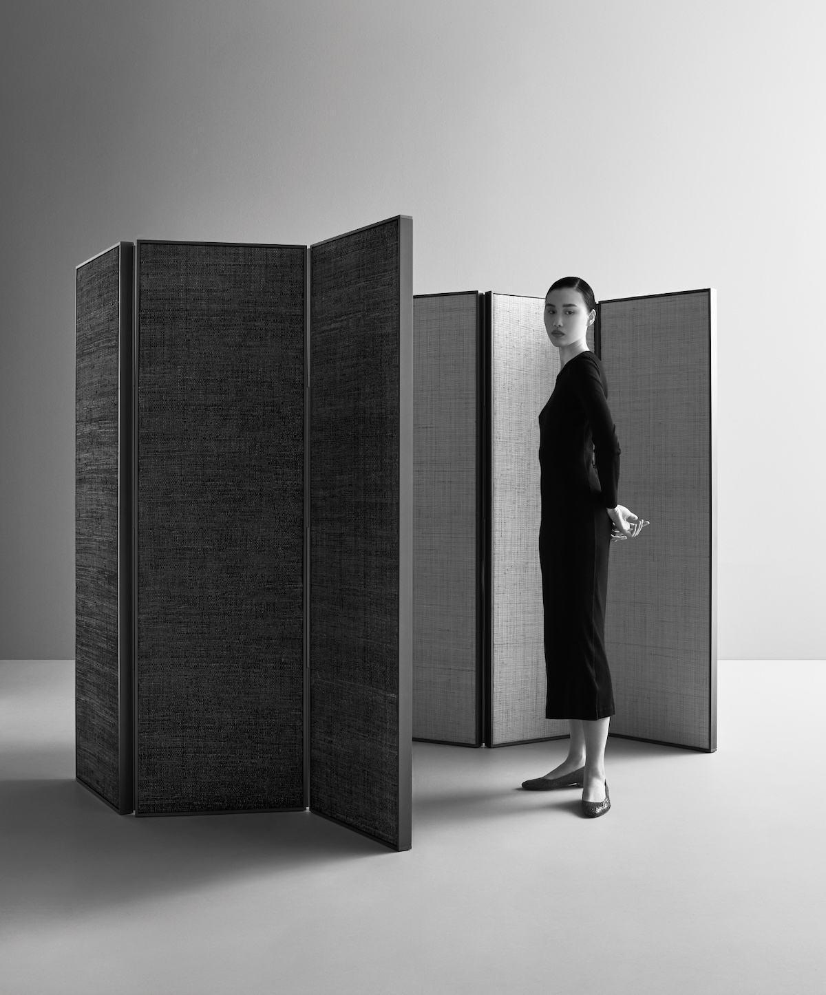 Das minimalistische, von Hotels inspirierte Bett Sileo mit abgerundetem Rahmen und hohem Kopfteil für ultimativen Komfort, sowie der ergänzende Paravent Privatus aus handgefertigtem Bast und Bananenblattstoff dahinter – und unten im Bild