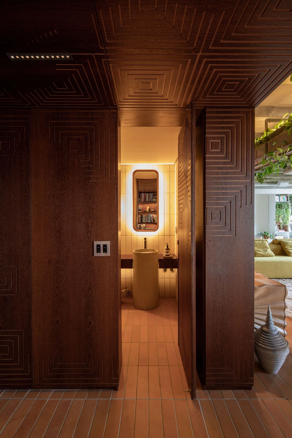 The Varanda Apartment has a feel of an ancient jungle civilisation, focusing on soft lighting reflected on dark wood surfaces and glinting through decorative vinery. Photo: Maíra Acayaba