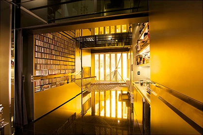 The walls in the apartment's main room, awash in yellow because of tinted windows, are pushed against the wall to the left to create an open space, with CDs to the left and the desk to the right.
