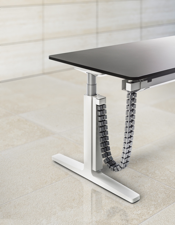 Cables run through a vertical cableway mounted to the leg without tools and then via a cable chain to a fold-down cable tray beneath the front edge of the table