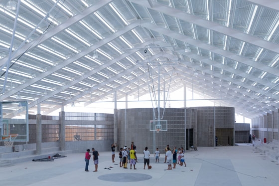 At the heart of the open building lies the sports area with its surrounding spectators’ stands. The various round function and sports rooms adjoin the central space on its short sides; photo: Iwan Baan